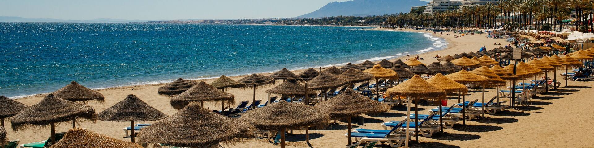 A beach with thatched umbrellas, sun loungers, and a clear blue sea.
