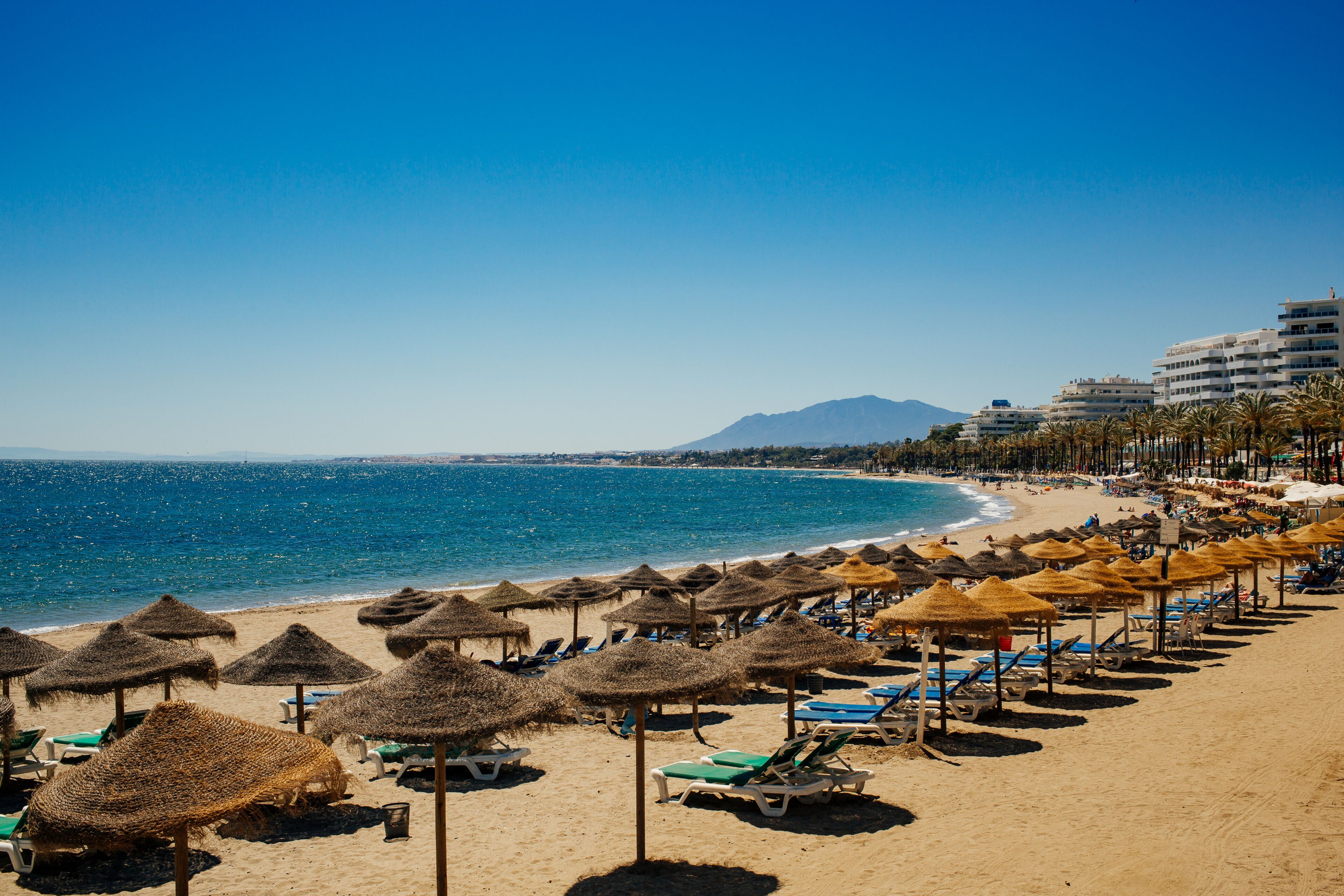A beach with thatched umbrellas, sun loungers, and a clear blue sea.