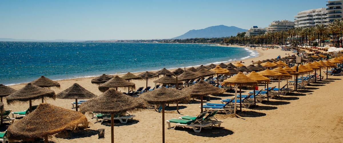 A beach with thatched umbrellas, sun loungers, and a clear blue sea.