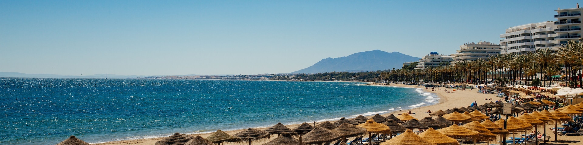 A beach with thatched umbrellas, sun loungers, and a clear blue sea.