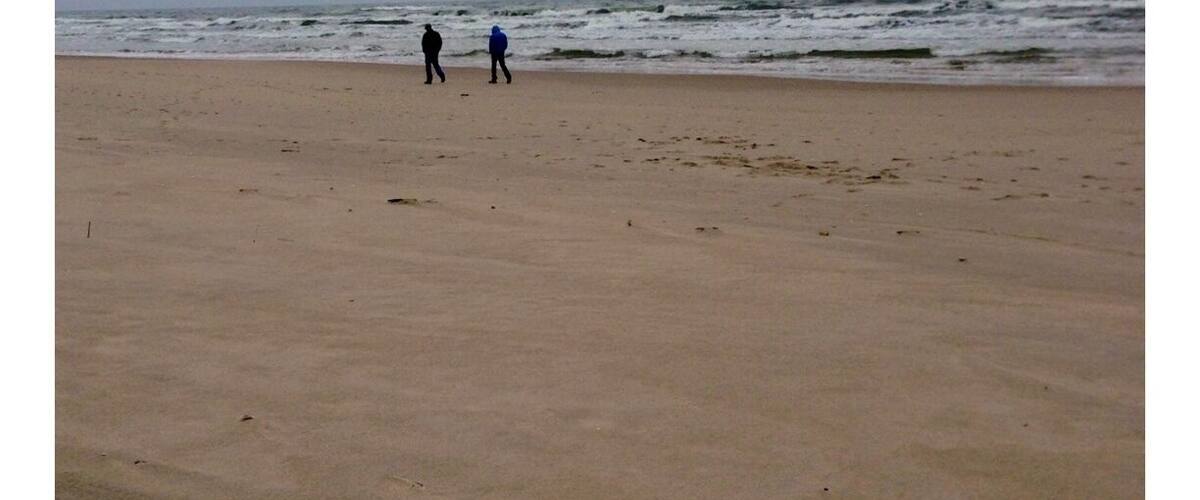 A beach with two people walking along the shore under a cloudy sky.