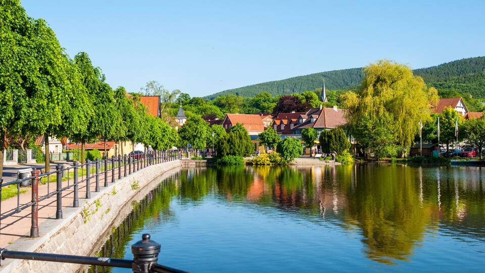 A calm river with a stone embankment, lush greenery, and traditional houses with red roofs.