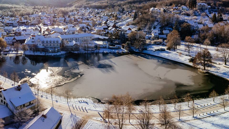 A snow-covered town with a frozen river, historic buildings, and a prominent castle-like structure.