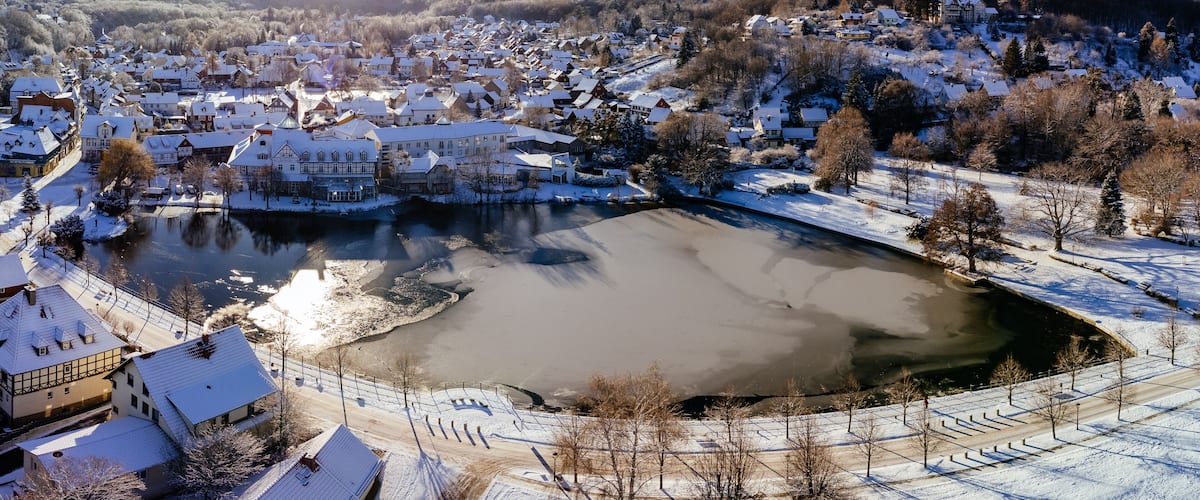 A snow-covered town with a frozen river, historic buildings, and a prominent castle-like structure.