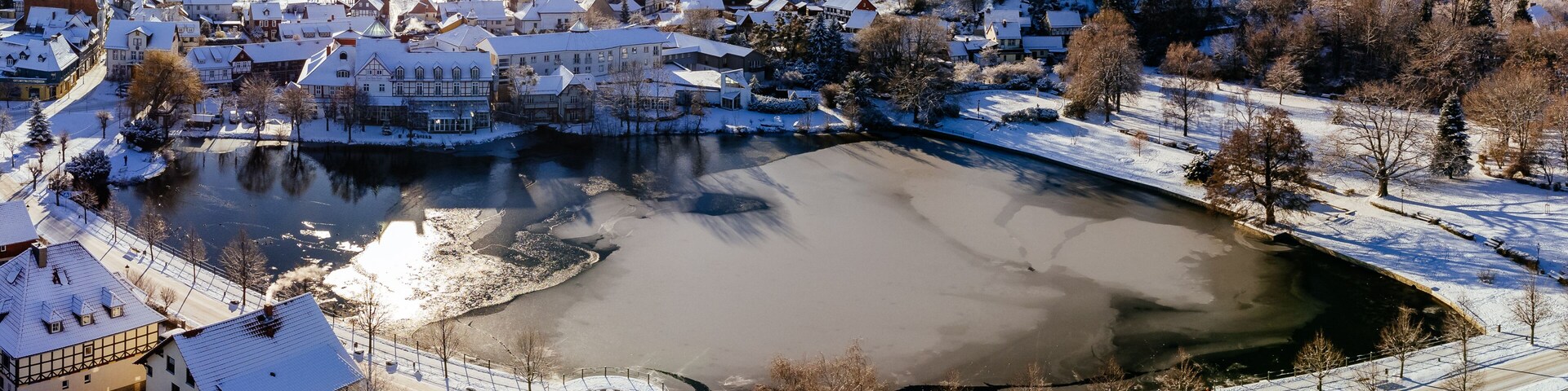 A snow-covered town with a frozen river, historic buildings, and a prominent castle-like structure.