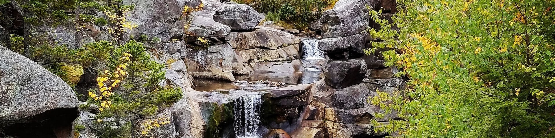 A waterfall cascading over rocks in a forest with autumn foliage.