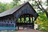 A wooden covered bridge with a bench in front.