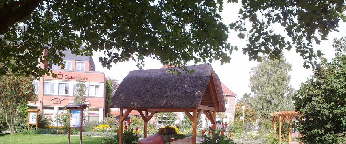 A garden with a wooden gazebo, brick pathway, and flowering beds.