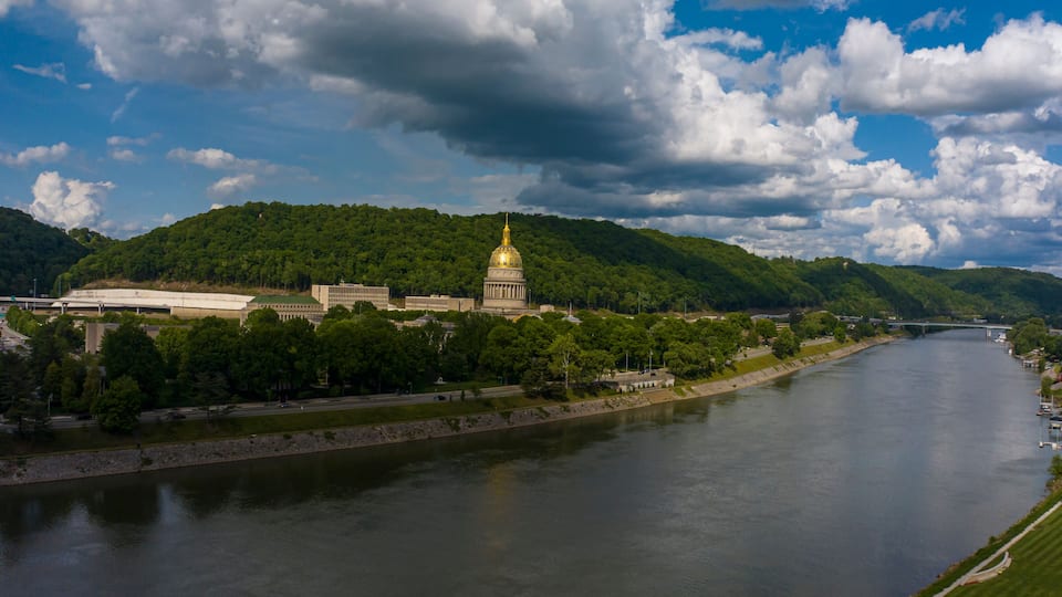 A river with a large building with a golden dome, surrounded by green hills and trees.