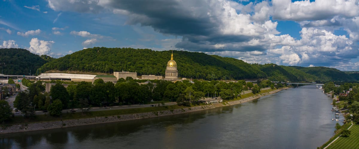 A river with a large building with a golden dome, surrounded by green hills and trees.