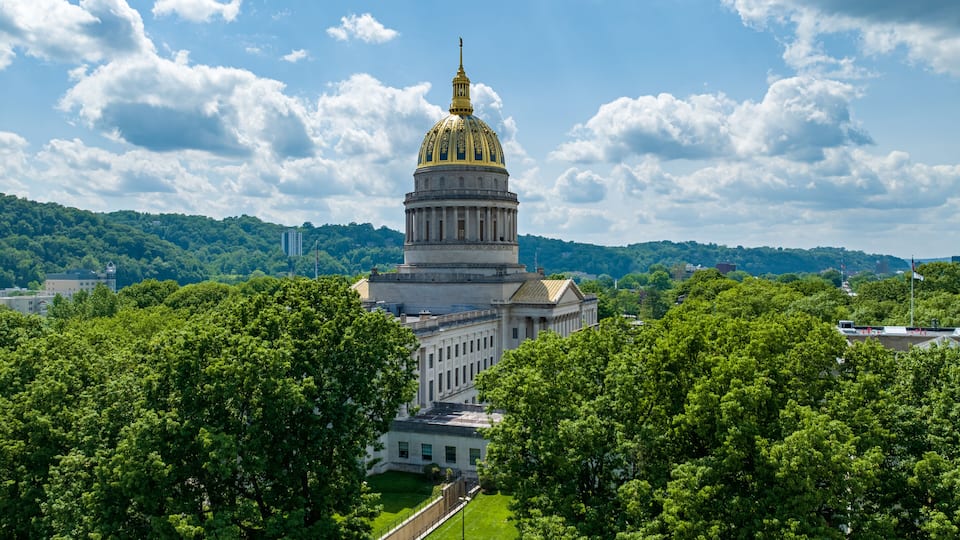 A large government building with a golden dome, surrounded by lush green trees and hills in the background.