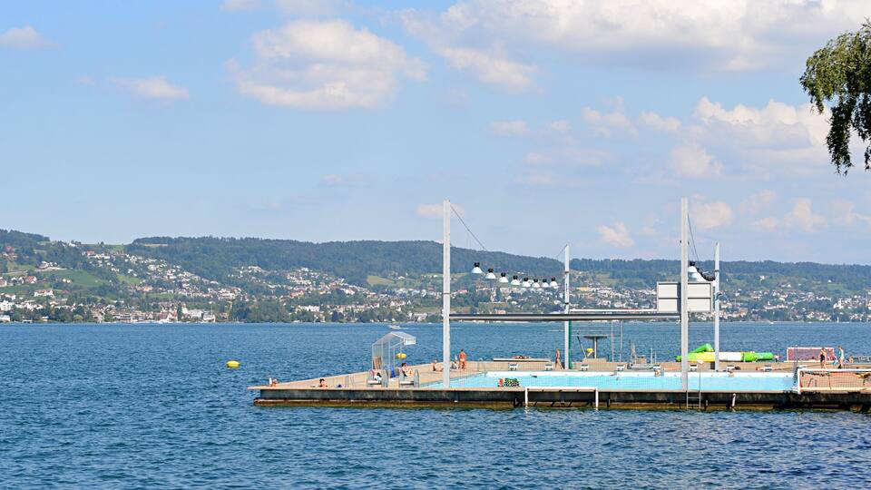A dock with a swimming pool, a boat, and a cityscape in the background.
