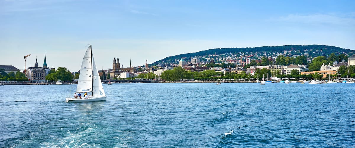 Un velero en un río con un paisaje urbano y una colina al fondo.