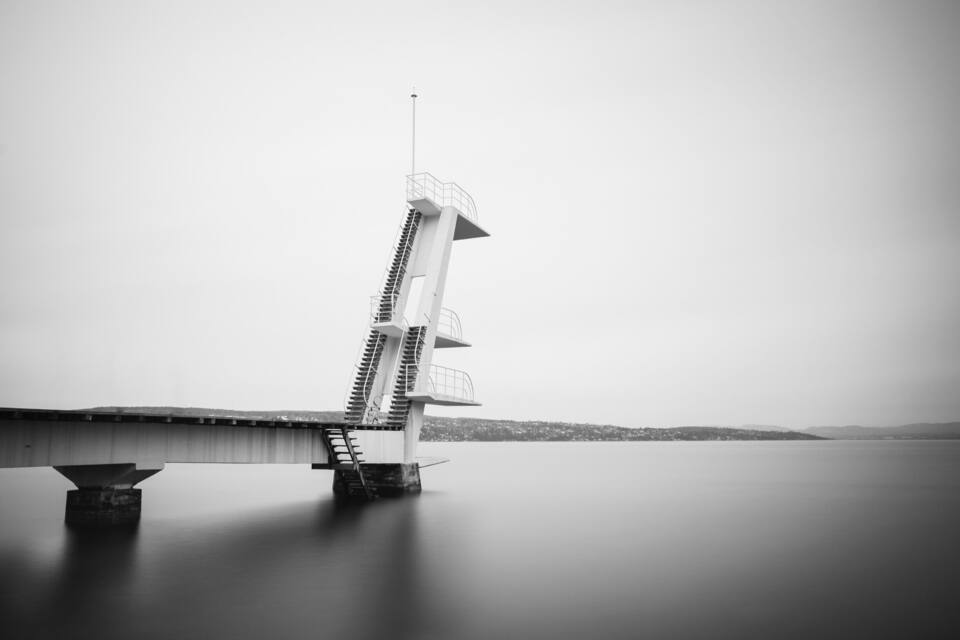A bridge with a unique leaning tower structure over a calm body of water.