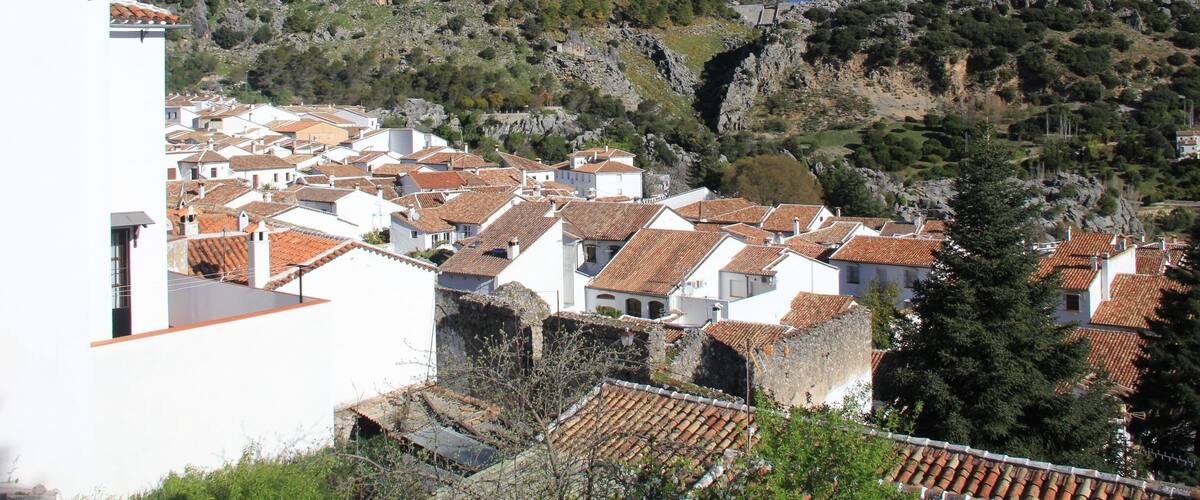 A coastal village with terracotta-roofed houses, a white church, and rocky hills in the background.