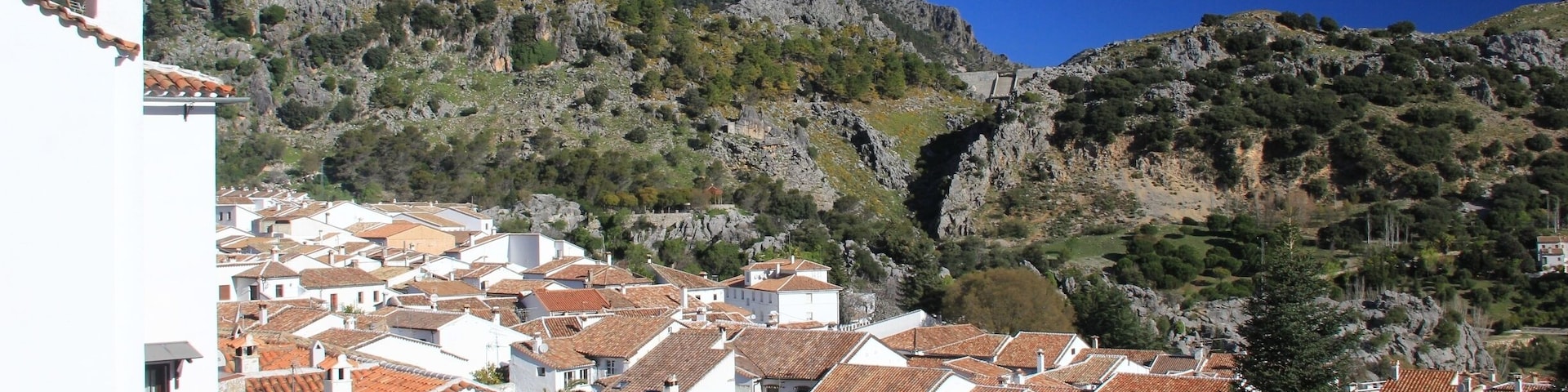 A coastal village with terracotta-roofed houses, a white church, and rocky hills in the background.