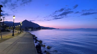 A waterfront promenade at dusk with street lamps and a mountain in the background.