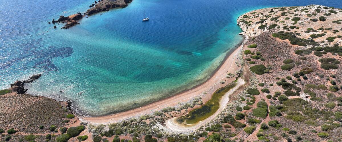 A coastal landscape with a clear blue sea, a small island with rocky terrain, and a sandy beach with sparse vegetation.