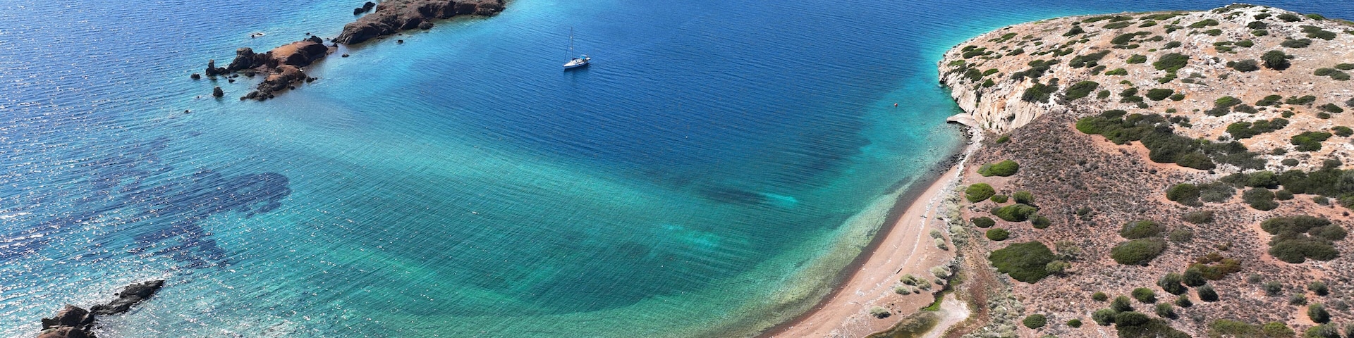 A coastal landscape with a clear blue sea, a small island with rocky terrain, and a sandy beach with sparse vegetation.