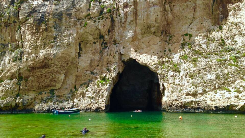 A rocky cliff with a cave entrance and clear green water.