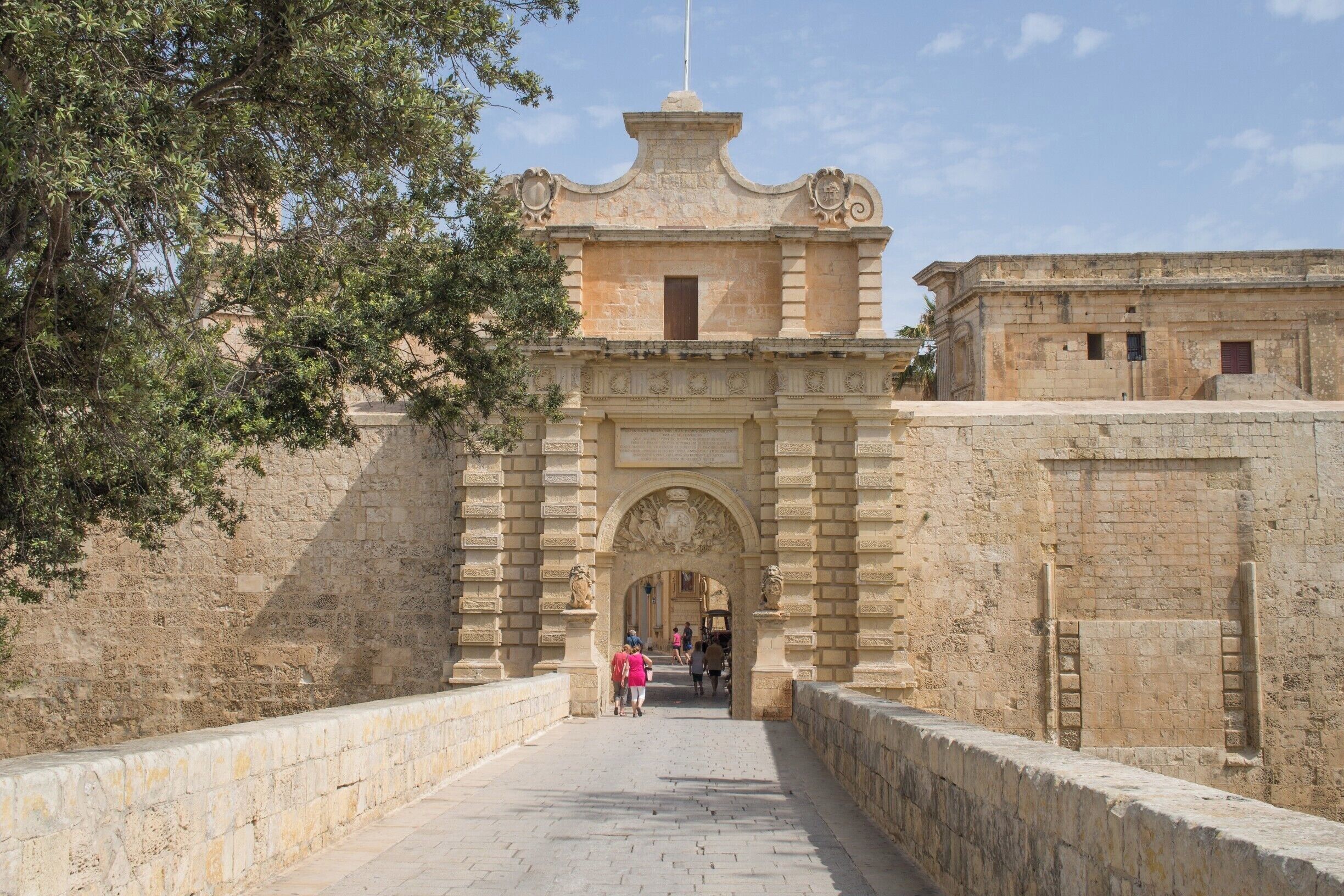 An old stone building with an ornate archway, a flagpole, and a paved walkway.