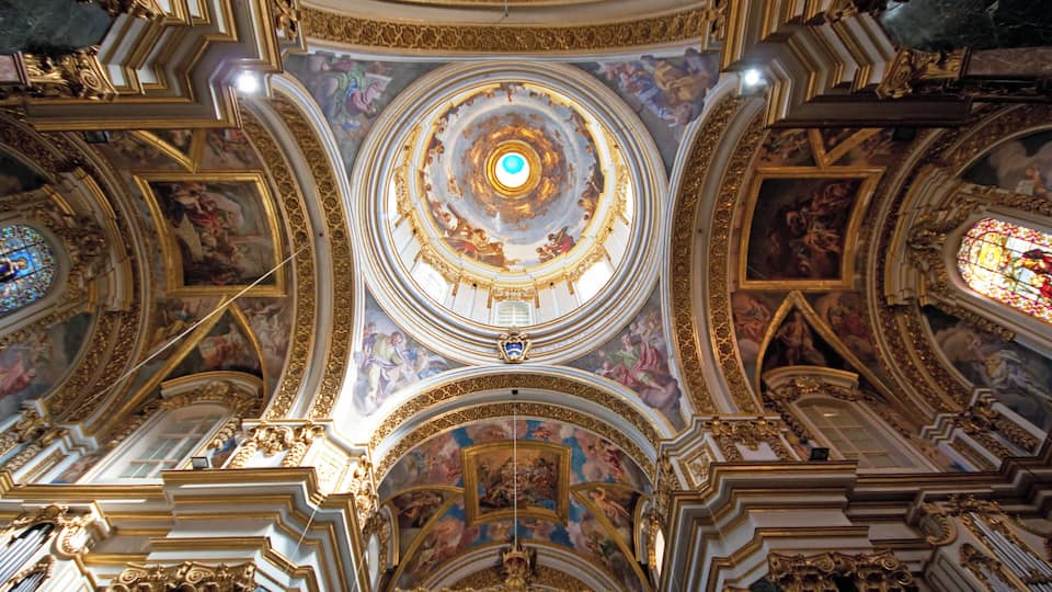 A grand cathedral interior with ornate gold detailing, a central dome, and stained glass windows.
