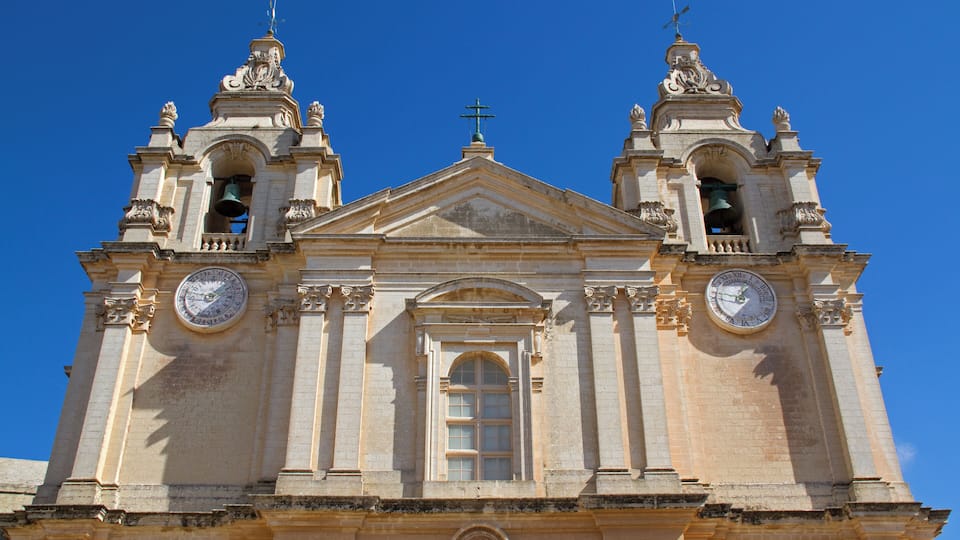 A historic church with two bell towers, a central dome, and a large clock on each tower.