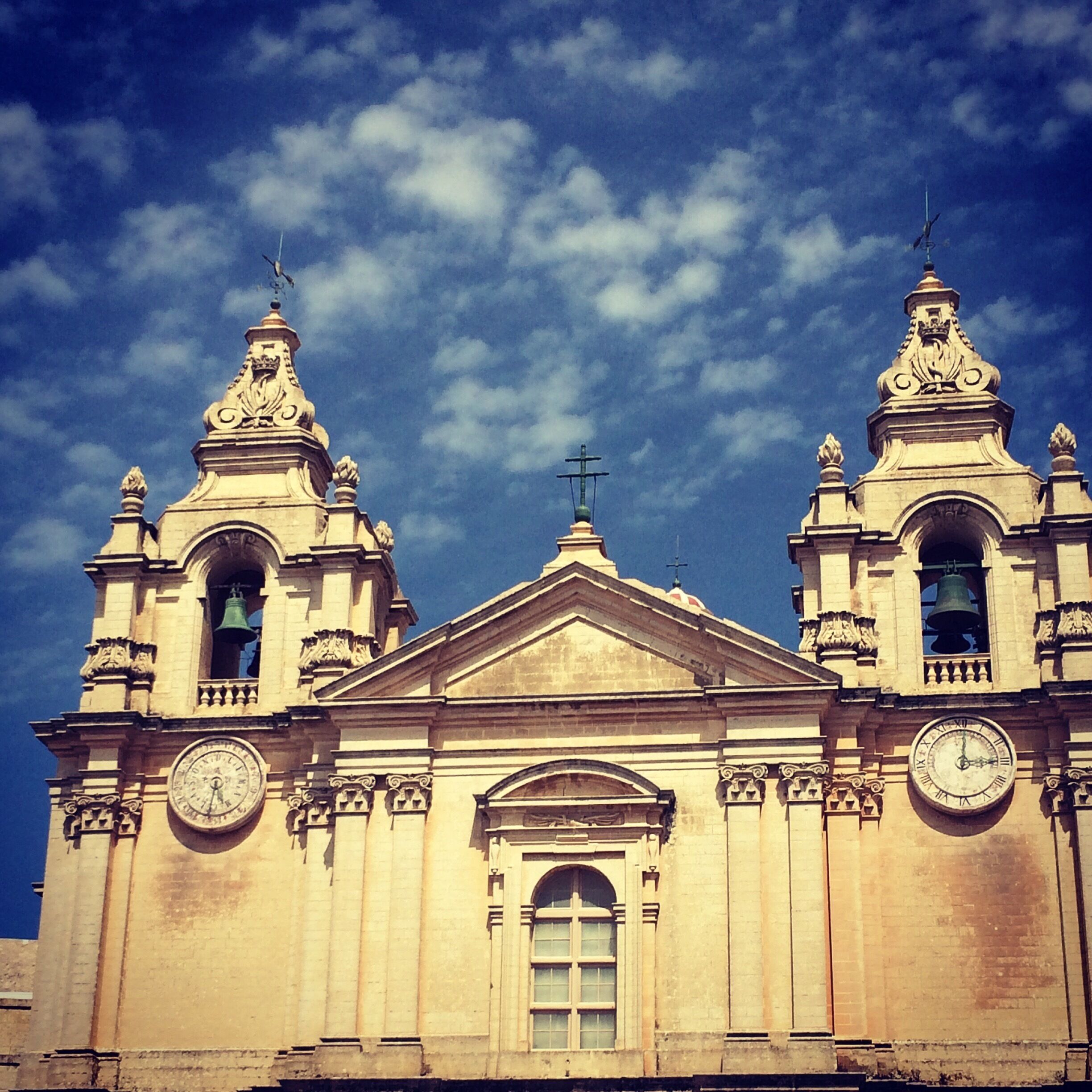 A historic church with two bell towers, a central dome, and a clock on each tower.