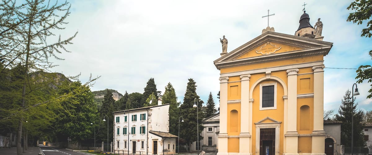 A yellow church with a statue on top and a white building with green windows in the background.
