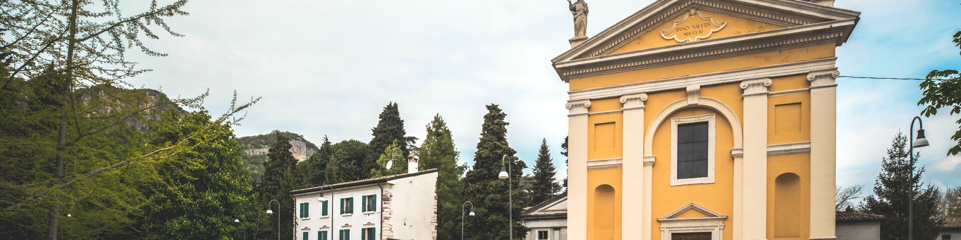 A yellow church with a statue on top and a white building with green windows in the background.