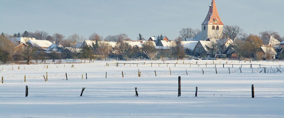 A snow-covered field with a church and residential buildings in the background.