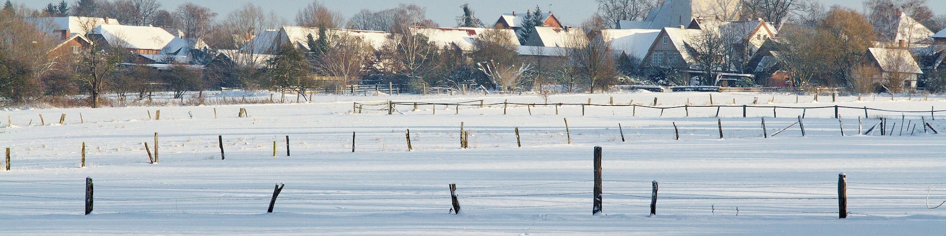 A snow-covered field with a church and residential buildings in the background.