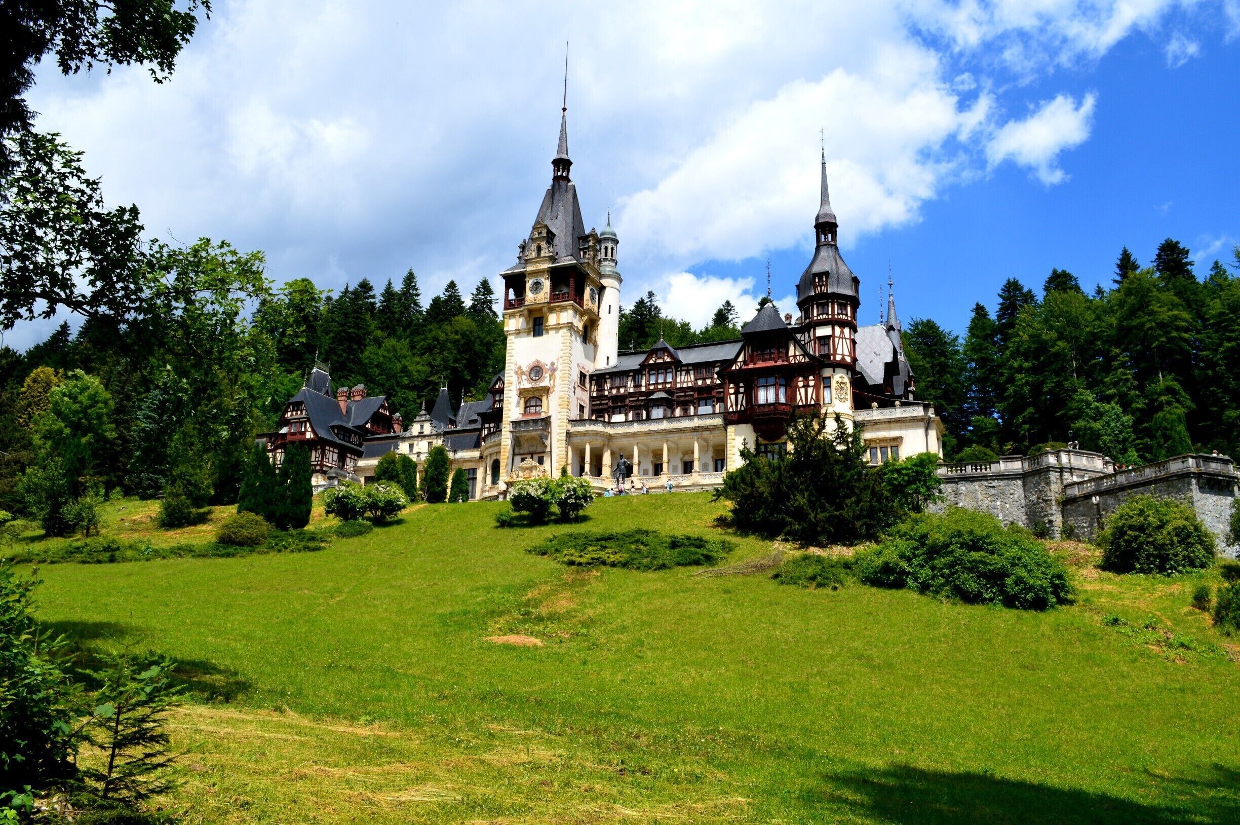 A large, historic castle surrounded by lush greenery and a clear blue sky.