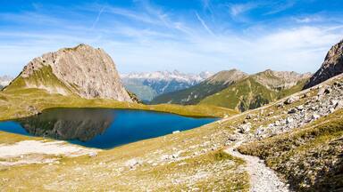 A mountainous landscape with a clear blue lake surrounded by rocky terrain and sparse vegetation.