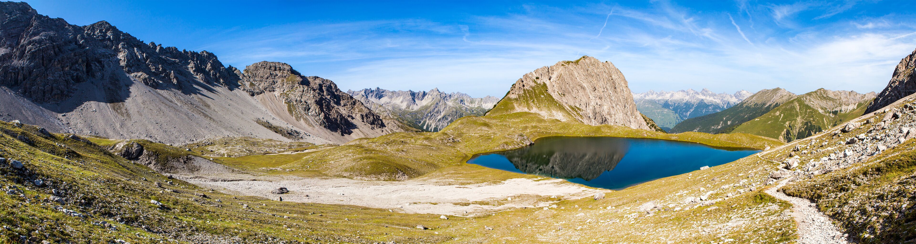A mountainous landscape with a clear blue lake surrounded by rocky terrain and sparse vegetation.