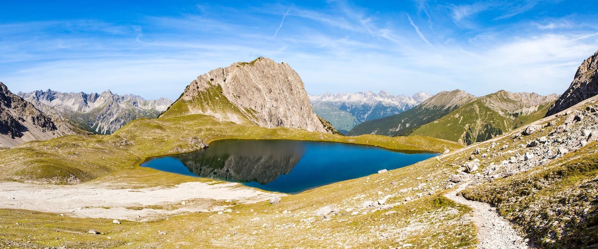 A mountainous landscape with a clear blue lake surrounded by rocky terrain and sparse vegetation.