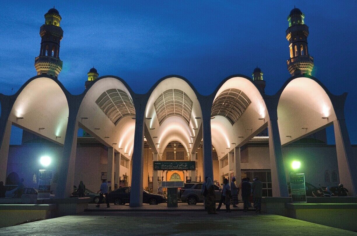 A mosque with large arched domes and minarets, illuminated at dusk.