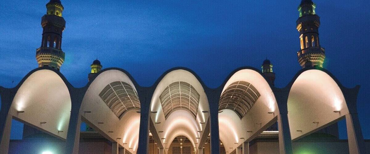 A mosque with large arched domes and minarets, illuminated at dusk.