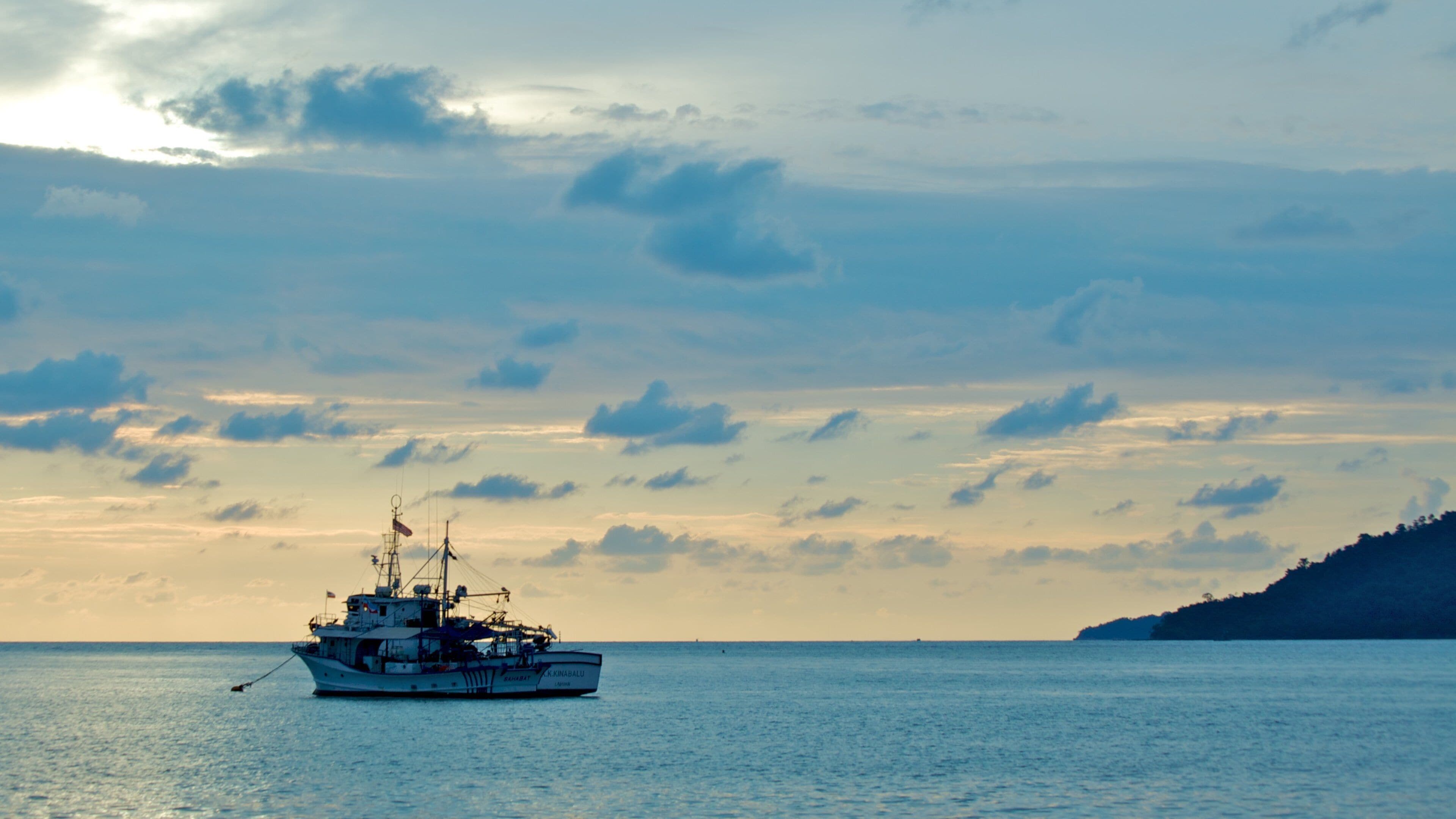 A fishing boat on calm waters with a cloudy sky and a distant landmass.