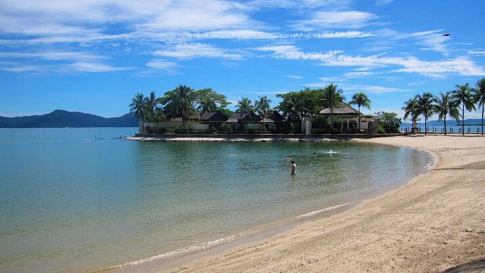 A tropical beach with clear water, palm trees, and a resort in the background.