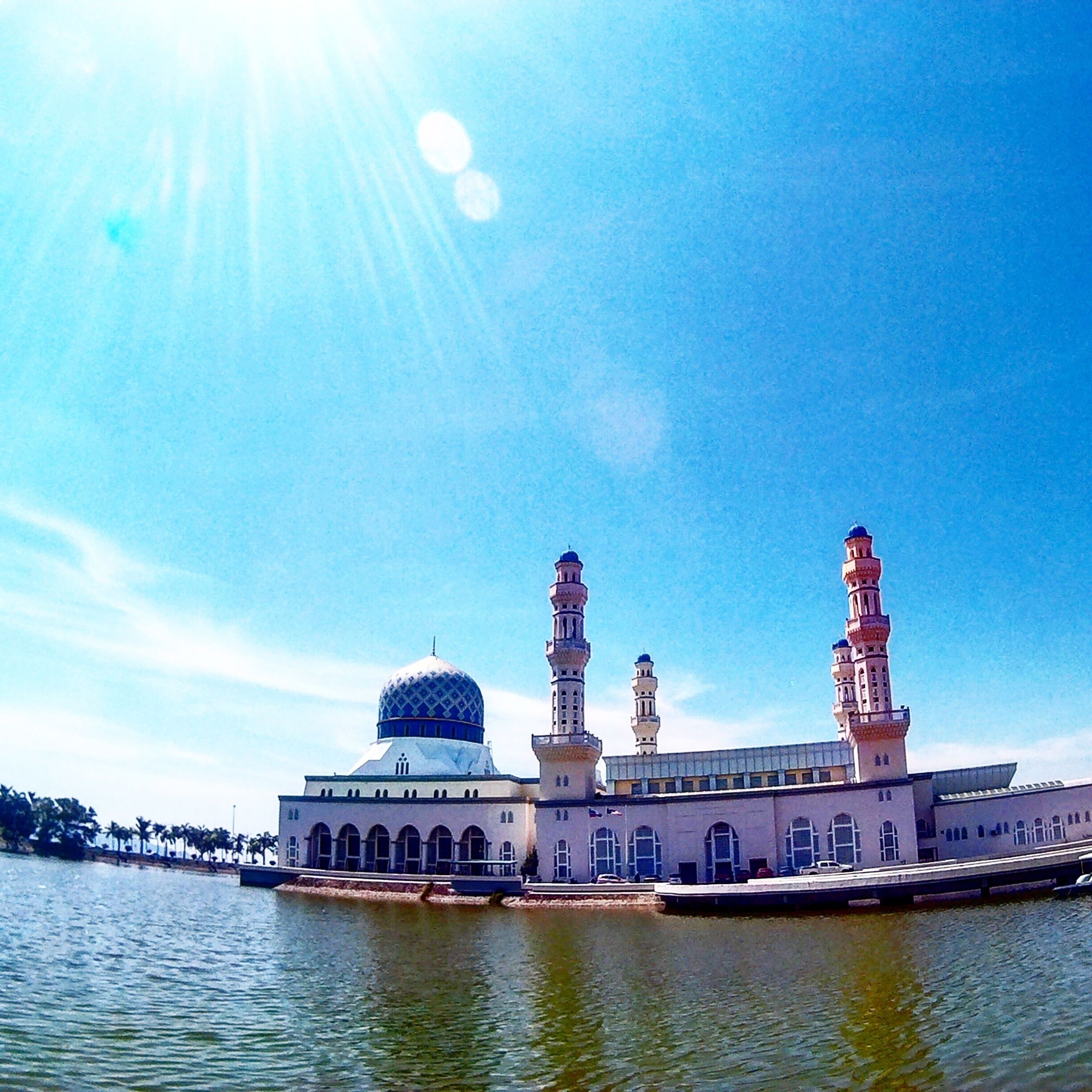 A mosque with a large dome and three minarets by a body of water.