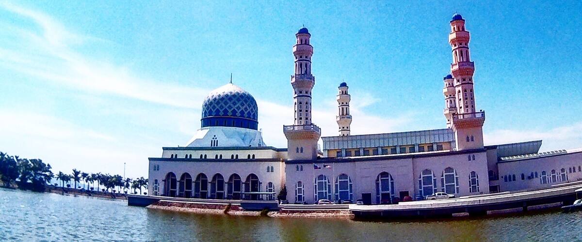A mosque with a large dome and three minarets by a body of water.
