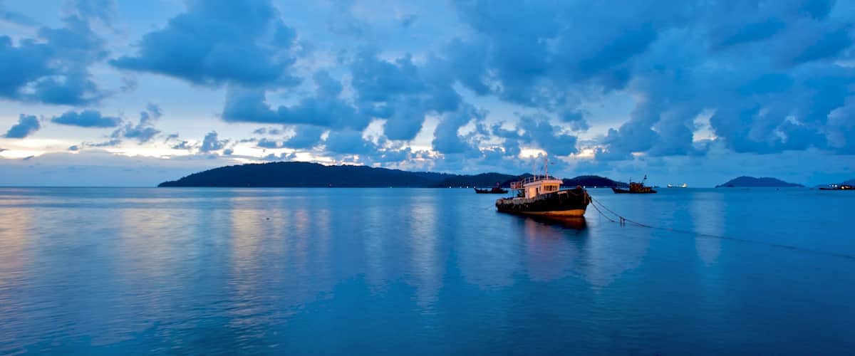 A calm sea with a boat anchored near a small island.