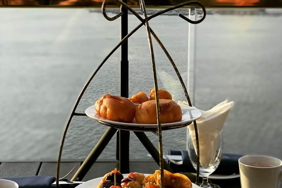 A table with a plate of food, a cup of coffee, and a view of a lake.