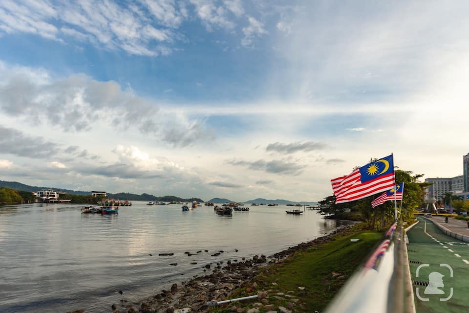 Une rivière avec des bateaux, un pont et les drapeaux de la Malaisie et des États-Unis.