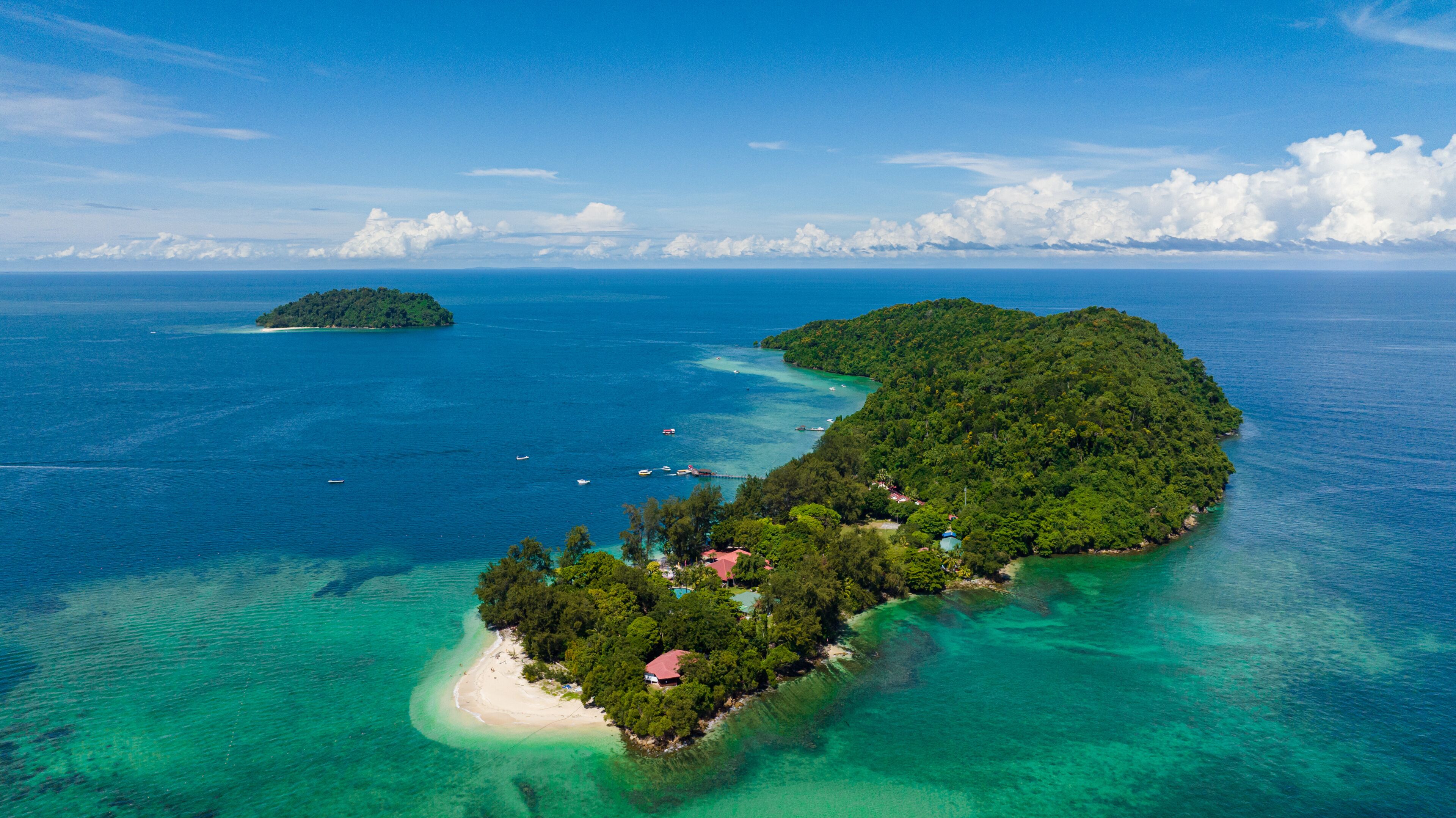 An aerial view of a tropical island with clear turquoise waters, a sandy beach, and lush greenery.