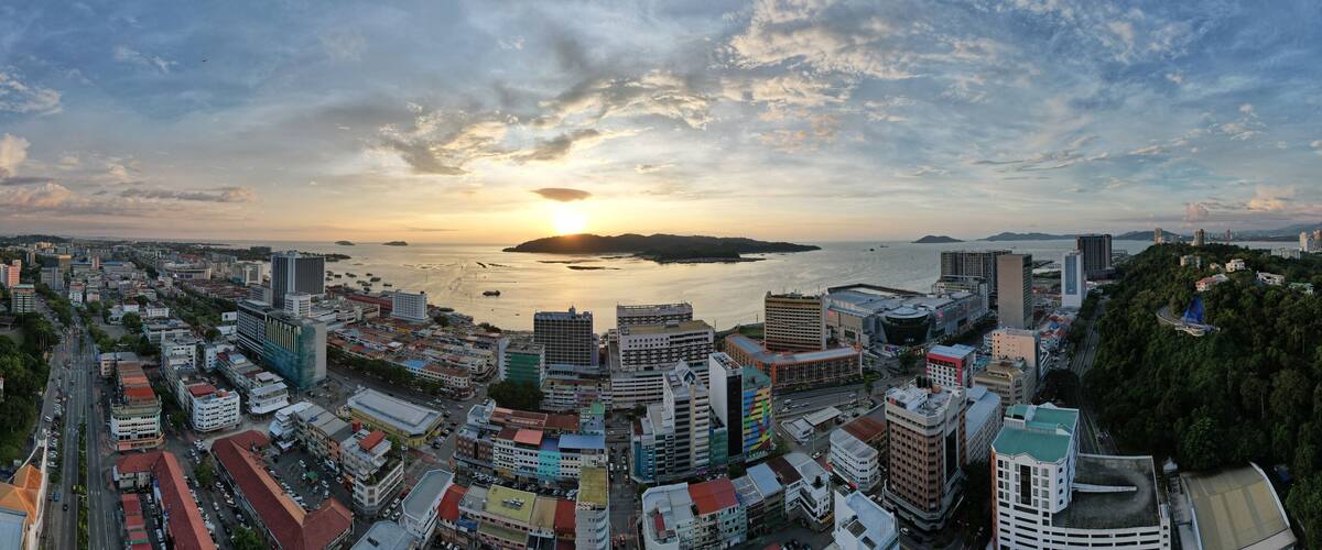 Un paysage urbain côtier avec un coucher de soleil sur la mer, mettant en valeur des bâtiments urbains denses et un ciel dégagé.
