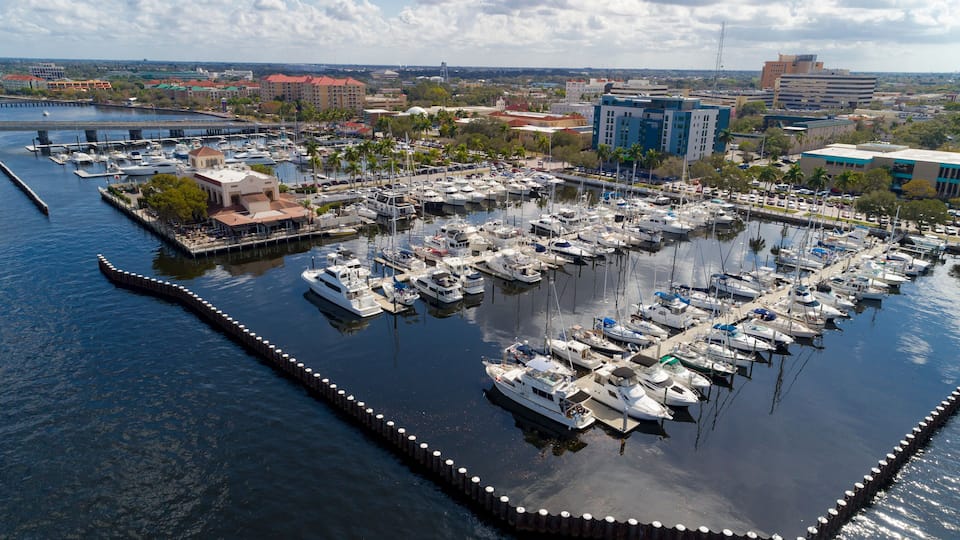 A marina with numerous boats docked, surrounded by buildings and palm trees.