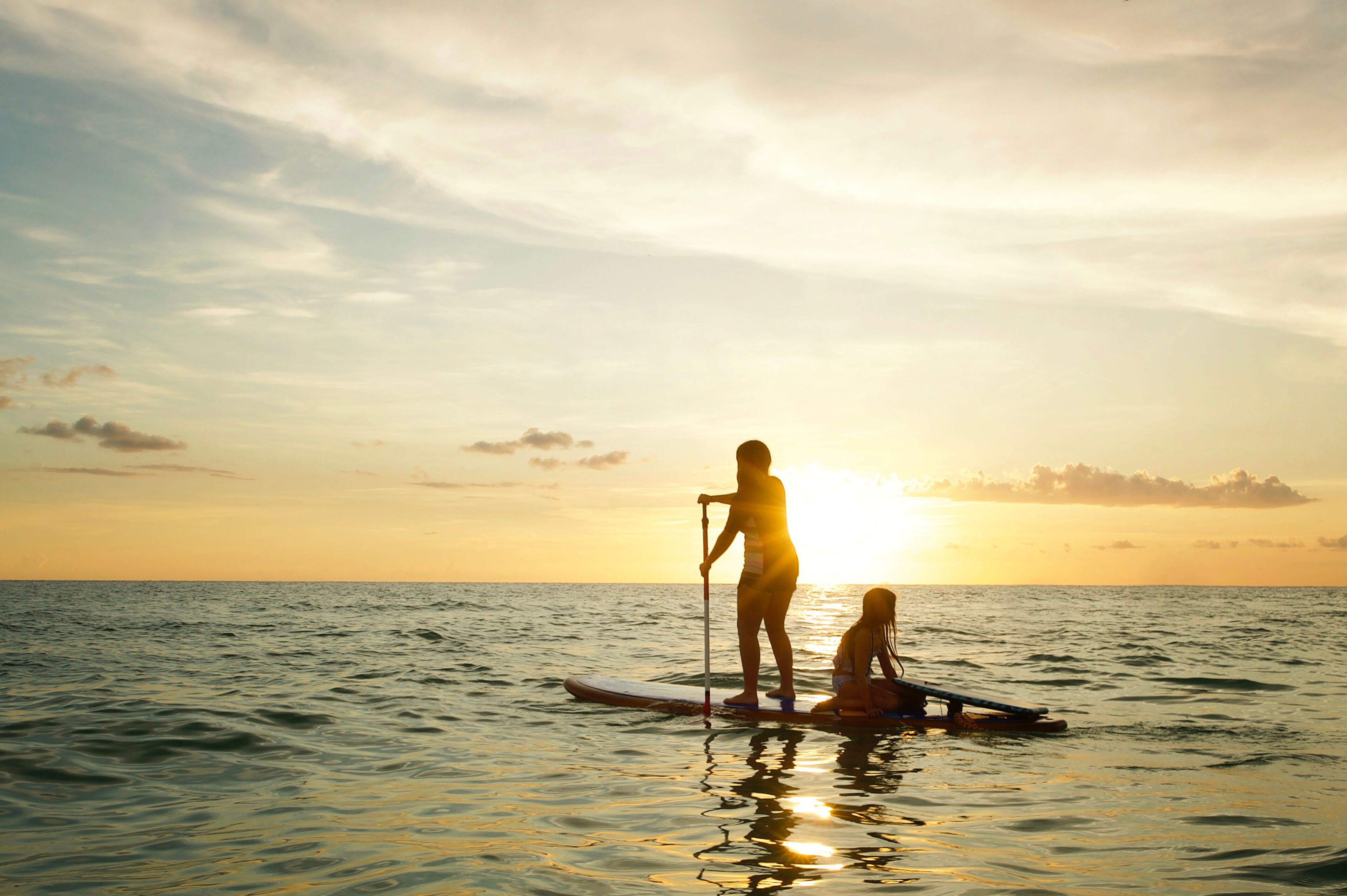 Two people paddleboarding on calm sea waters during sunset.