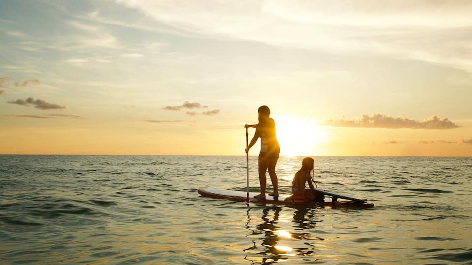Two people paddleboarding on calm sea waters during sunset.